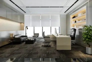 Modern executive office with a black leather seating area, white desk, computer, illuminated display shelves, large windows, and a potted tree.