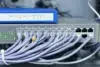 Network equipment with numerous Ethernet cables plugged into a 24-port switch beneath a blue wireless router.