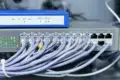 Network equipment with numerous Ethernet cables plugged into a 24-port switch beneath a blue wireless router.