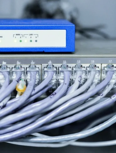 Network equipment with numerous Ethernet cables plugged into a 24-port switch beneath a blue wireless router.