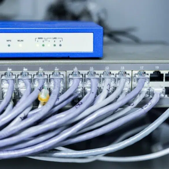 Network equipment with numerous Ethernet cables plugged into a 24-port switch beneath a blue wireless router.