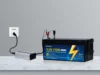A 12.8-volt 210Ah LiFePO4 battery connected to a silver inverter and wall outlet, with red and black clamps attached.