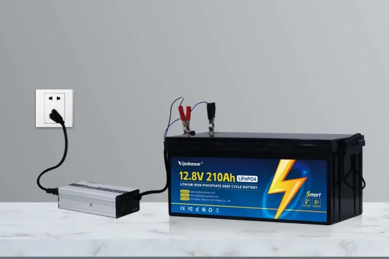 A 12.8-volt 210Ah LiFePO4 battery connected to a silver inverter and wall outlet, with red and black clamps attached.