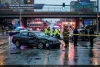 Rainy Rockford, Illinois crash scene: wrecked sedan, emergency responders, fire trucks and ambulance behind police tape under an overpass.