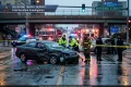 Rainy Rockford, Illinois crash scene: wrecked sedan, emergency responders, fire trucks and ambulance behind police tape under an overpass.