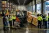 Industrial warehouse safety alert: investigators gather around an injured worker and forklift near fallen crates, behind yellow caution tape at Chesapeake port.