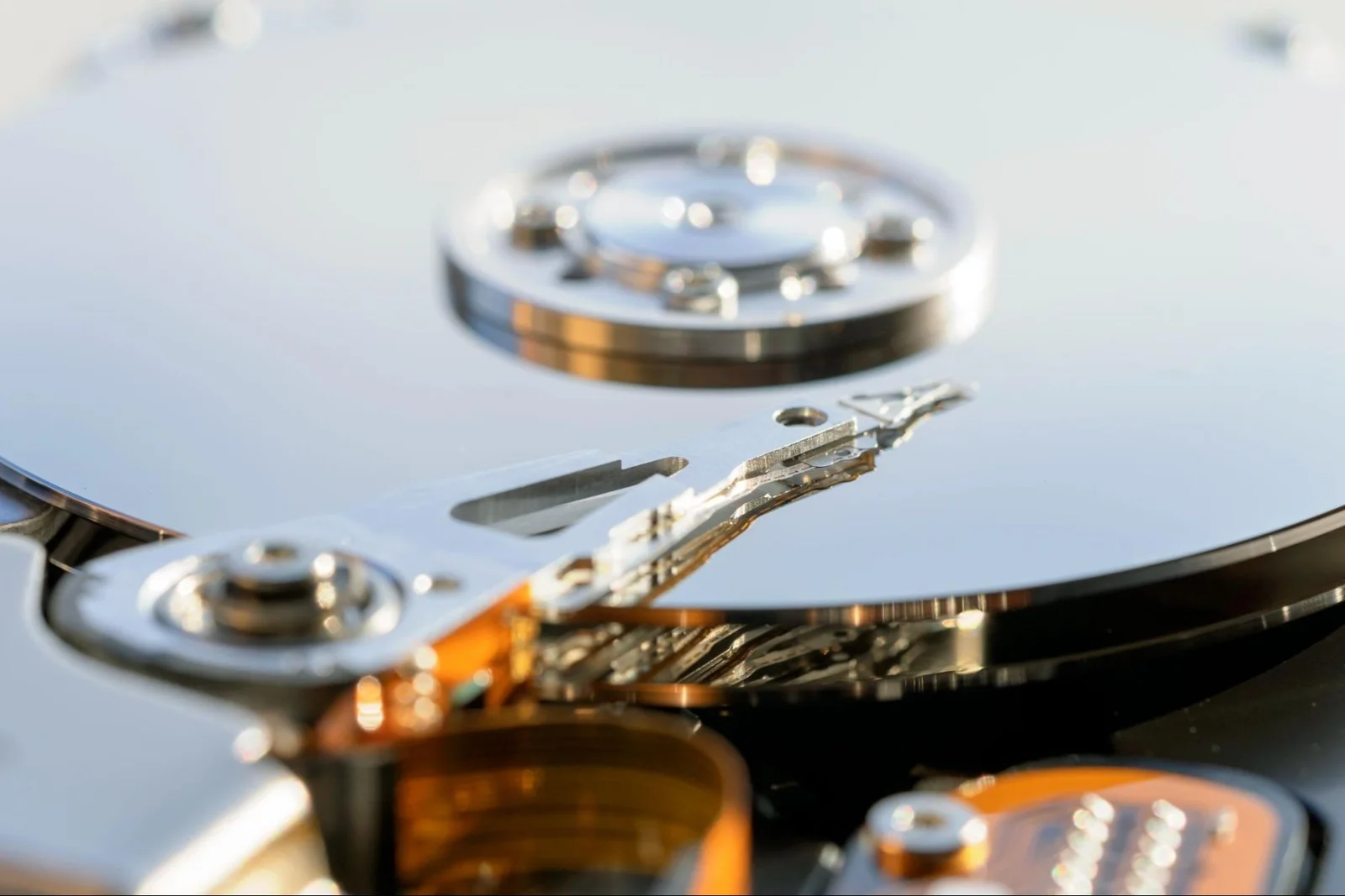 Close-up of an open hard disk drive, showing the shiny platter, read/write actuator arm, spindle, and intricate internal components.