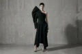 Model wearing a sculptural asymmetric black garment in a minimal studio setting