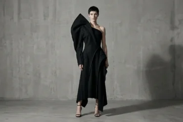 Model wearing a sculptural asymmetric black garment in a minimal studio setting